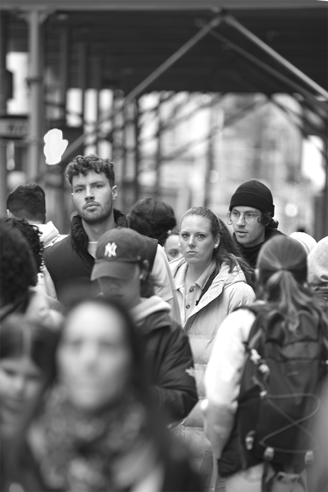 Black and white image of a man and woman looking directly at the view, the couple are in a crowd, East Village, Manhattan