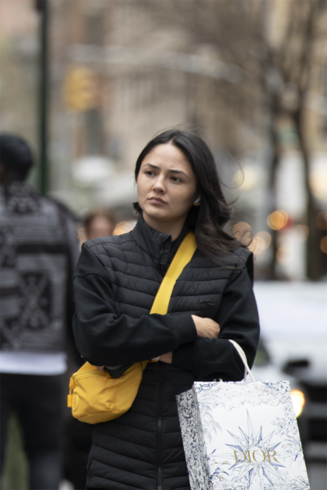 A woman wearing a black coat with bright yellow purse, and a Dior shopping bag, East Village, Manhattan